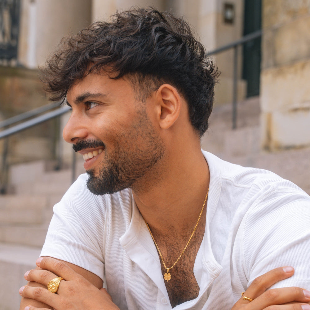 Man with a beard wearing a white shirt and gold necklace outdoors