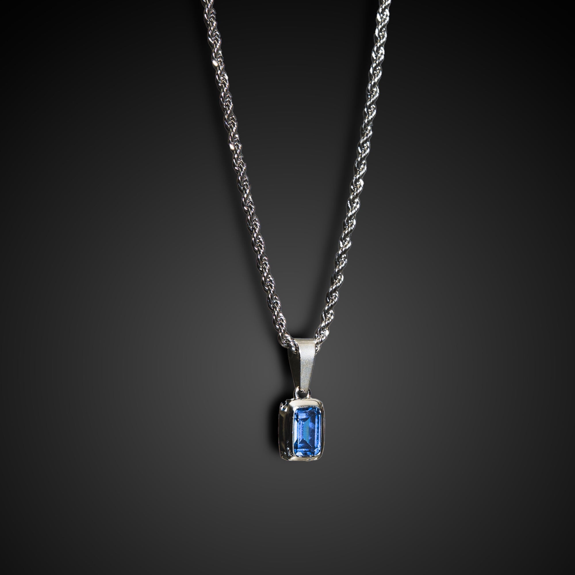 Silver necklace with a blue gemstone pendant on a dark background