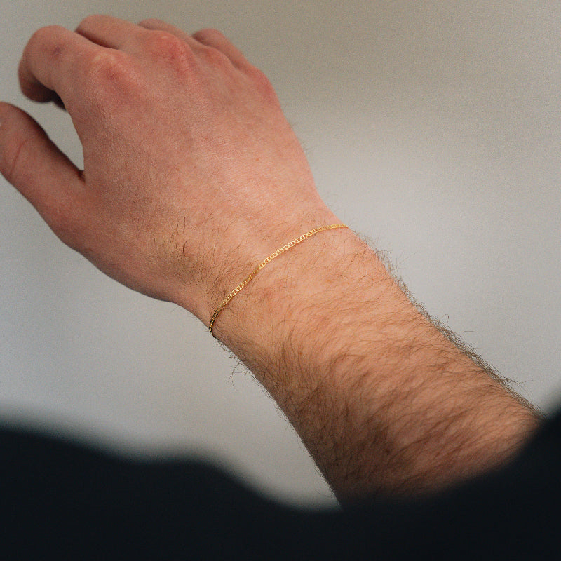 Gold bracelet on a person's wrist against a neutral background