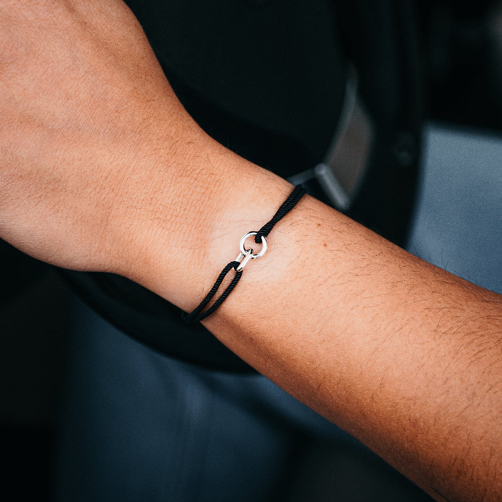 A person's wrist wearing a black driftwood-style bracelet with silver accents, adjustable to fit the wrist size.