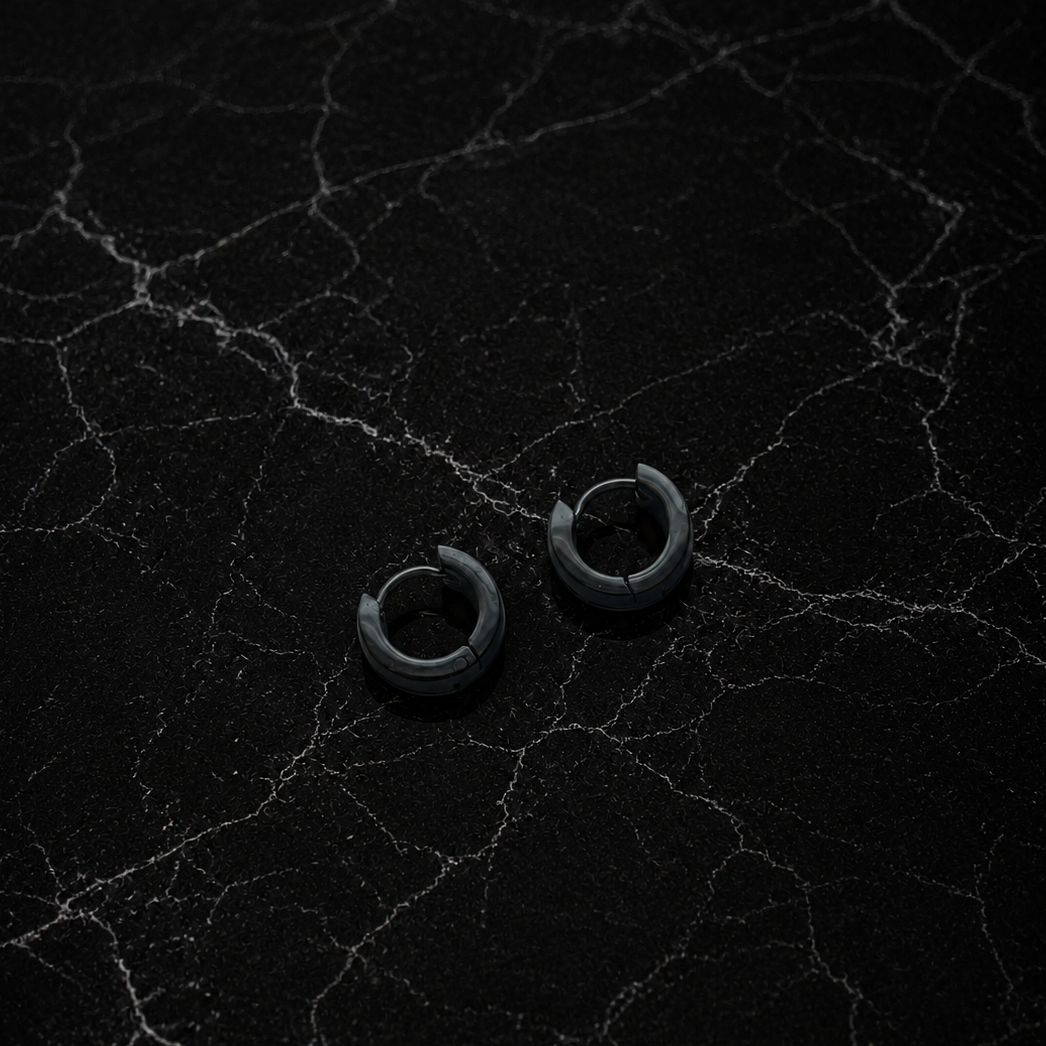 Pair of black hoop earrings on a textured black surface