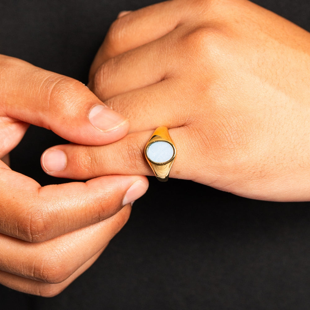 Close-up of a hand wearing a gold ring with a blue stone on a black background