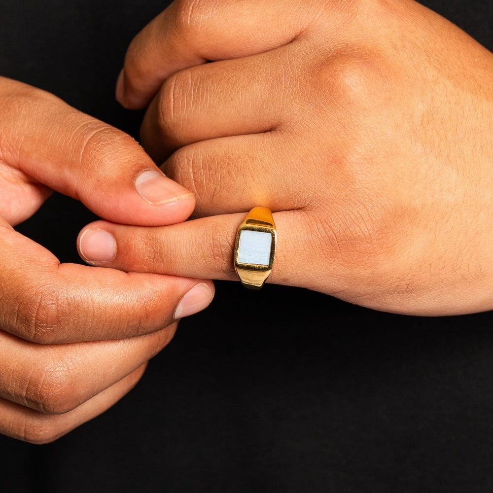 Gold ring with a stone on a person's finger against a black background