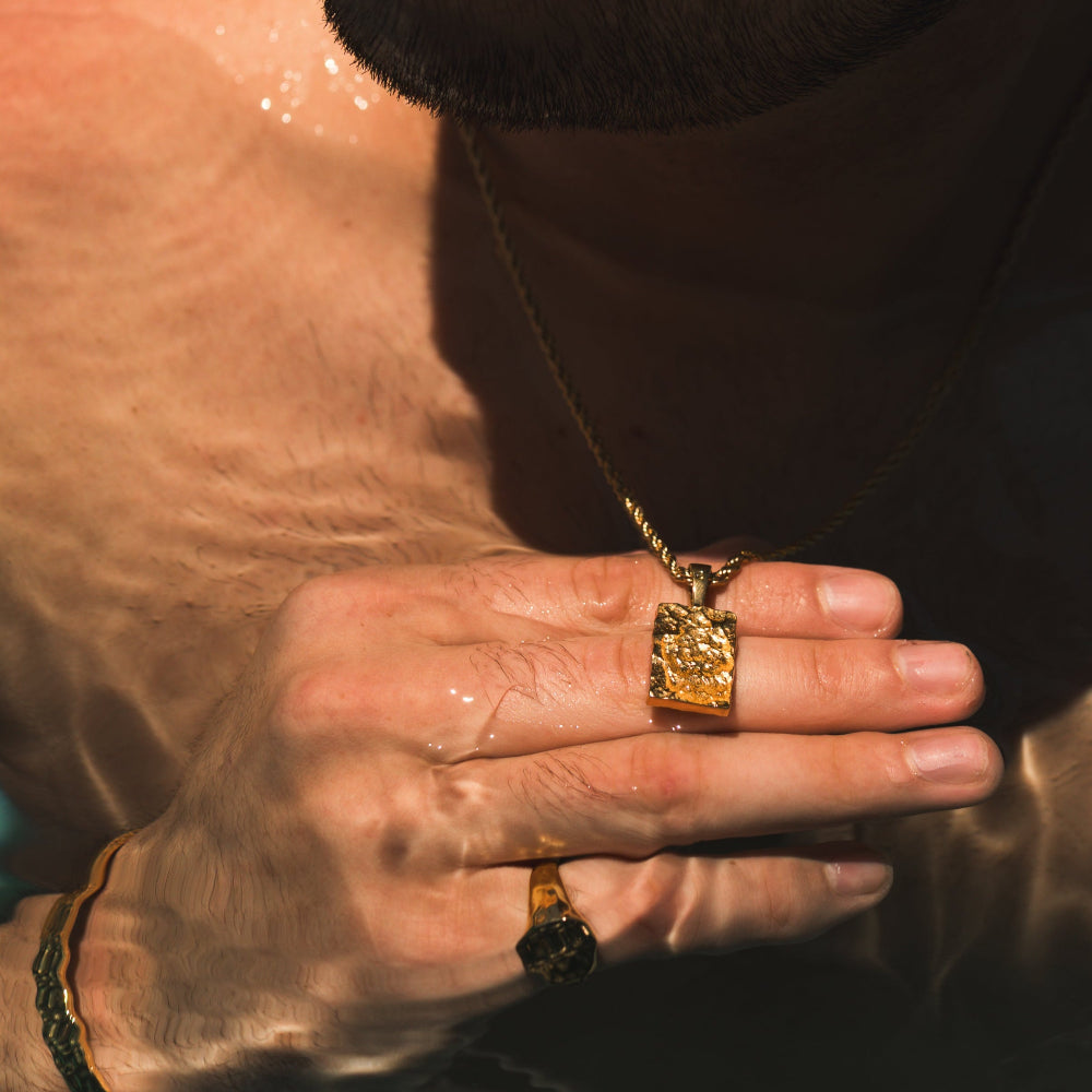 Close-up of a person's hand with gold jewelry in a reflective surface setting
