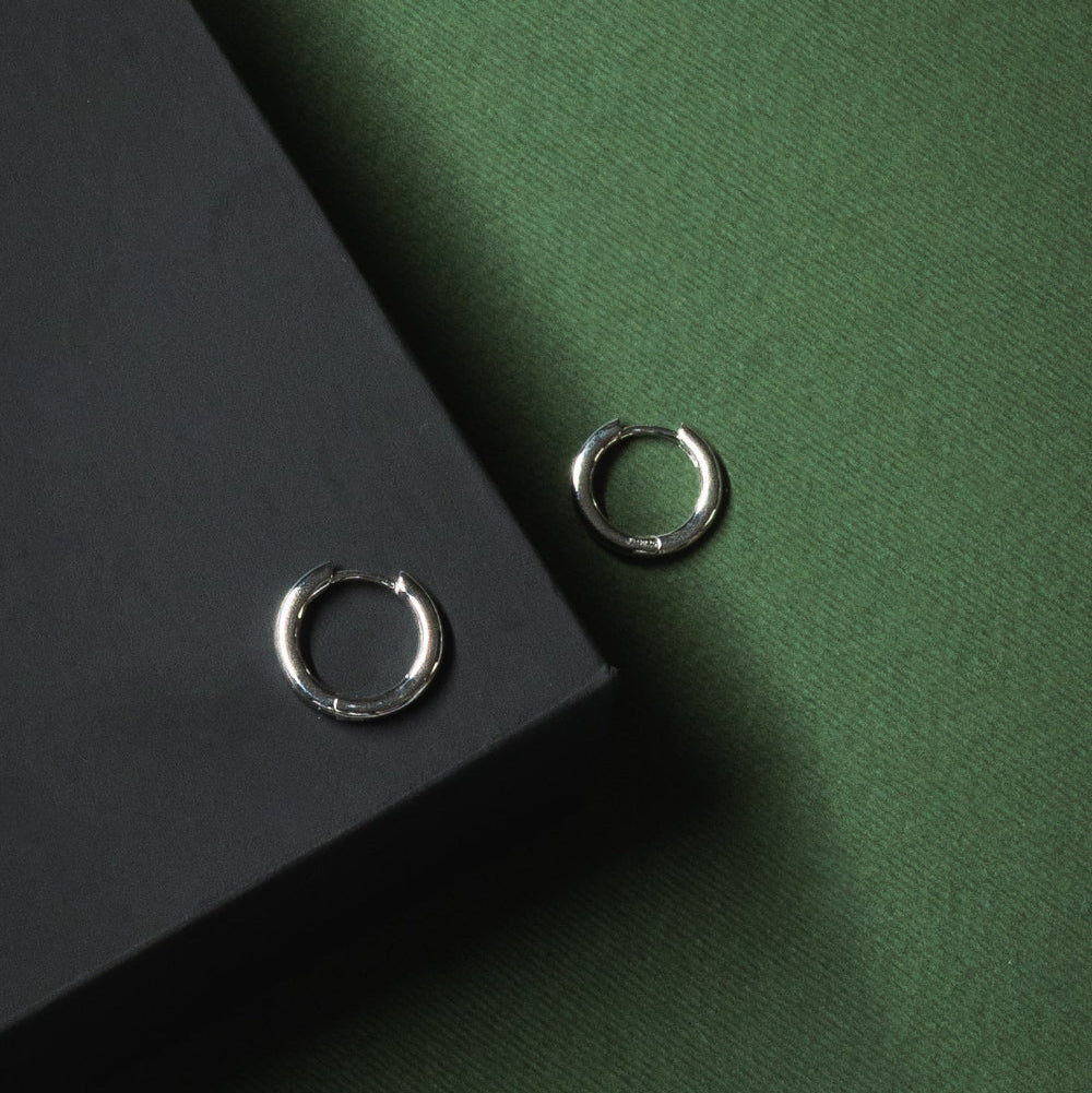 Two silver hoop earrings on a green and black background