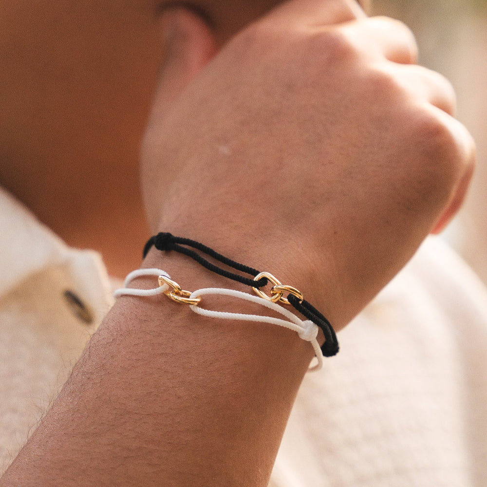 A person's wrist wearing a black and gold bracelet with interlocking nylon and sterling silver elements.