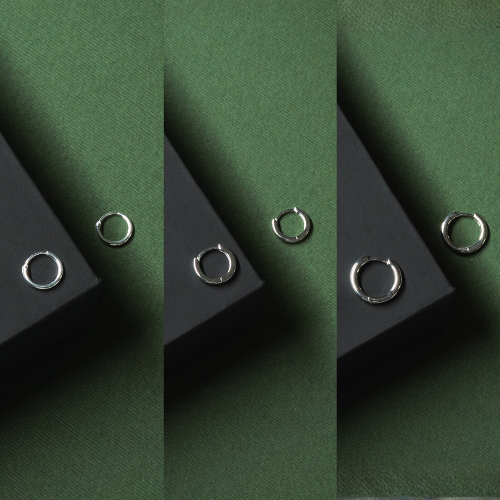 Silver hoop earrings on black stands against a green background