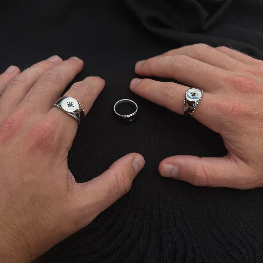 Two hands wearing silver rings with gemstones on a black background