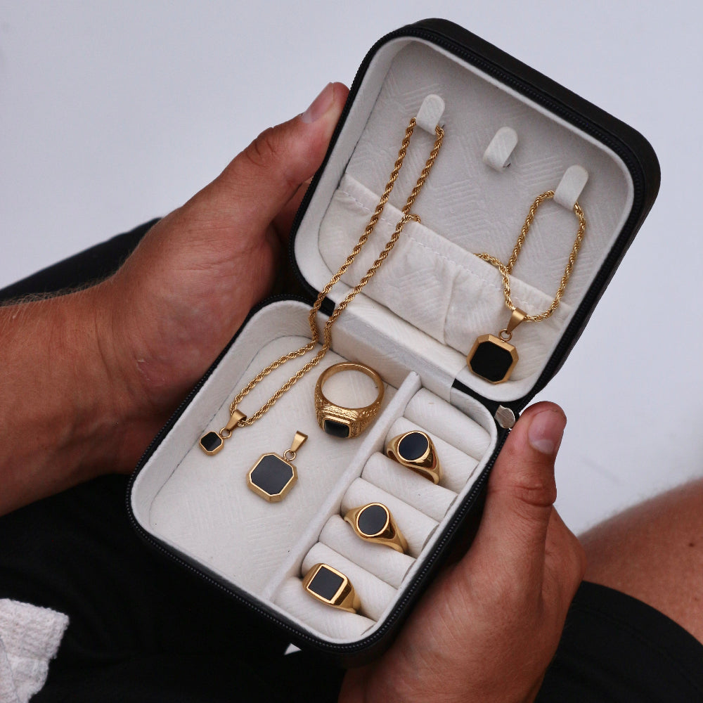 Jewelry set including necklaces and rings in an open jewelry box held by a person.