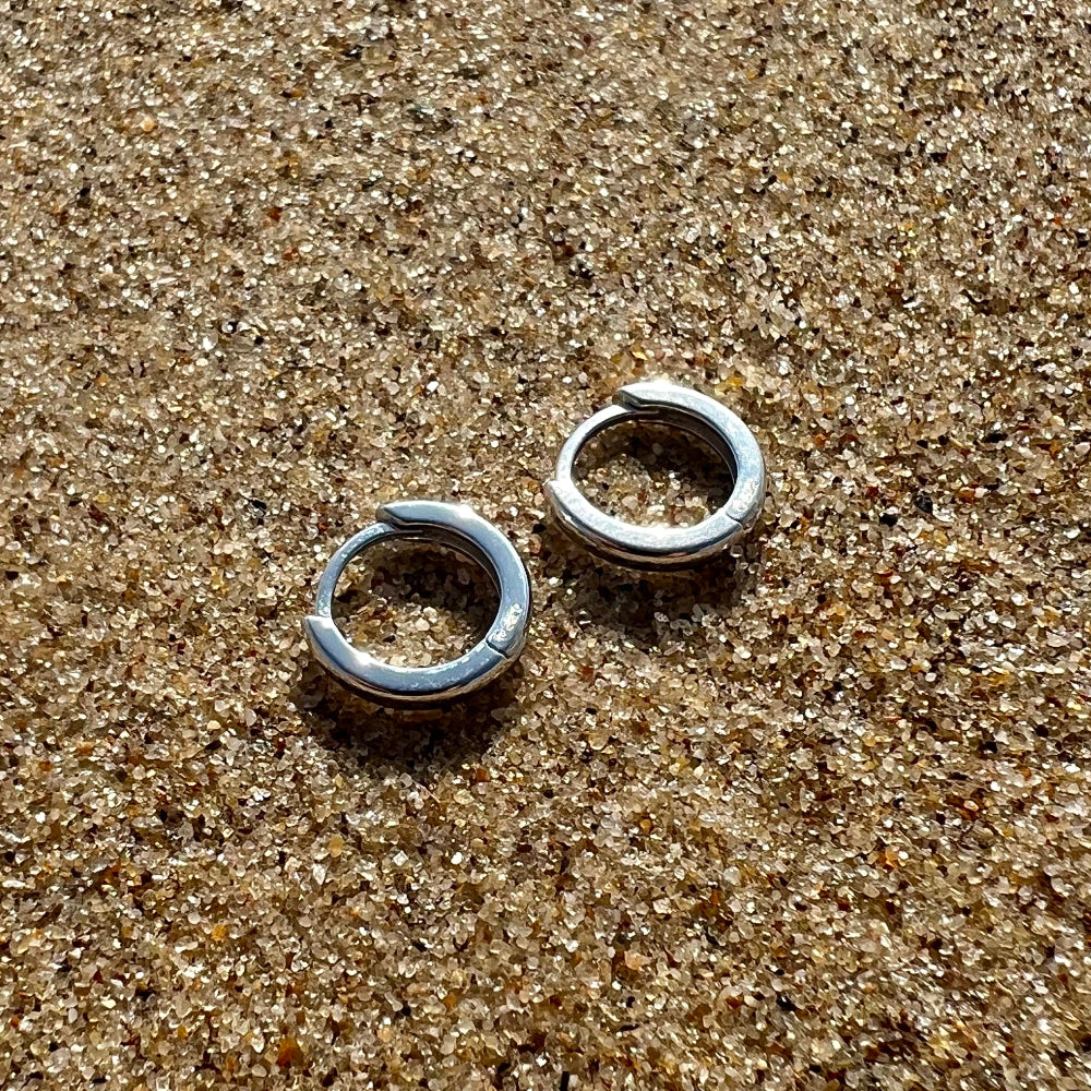Two silver hoop earrings on a sandy surface