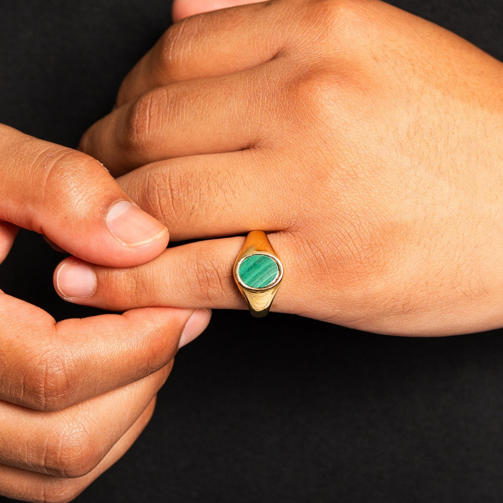 Hand wearing a gold ring with a green gemstone against a dark background