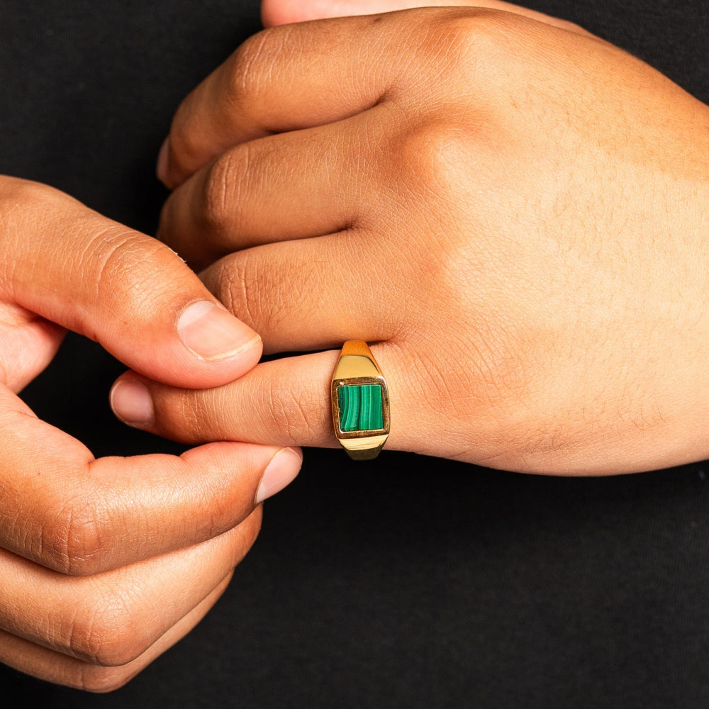 Gold ring with a green gemstone on a hand against a black background