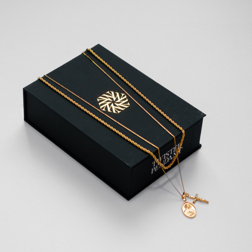 Gold necklace with a pendant on a black jewelry box with a brand logo.