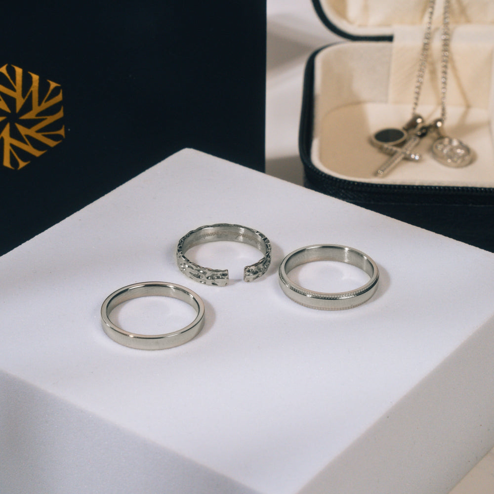Three silver rings on a white surface with a jewelry box in the background.