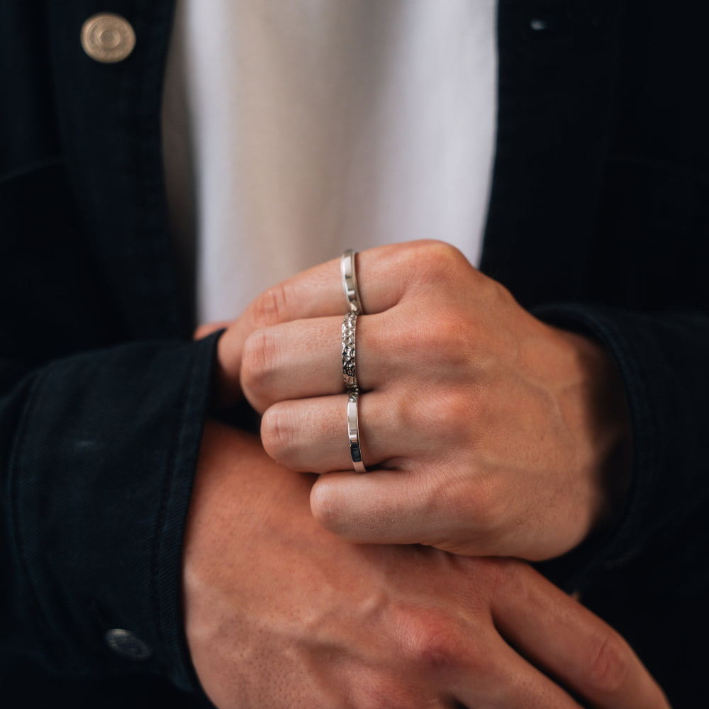 Close-up of a person's hands with silver rings on fingers, wearing a dark jacket.