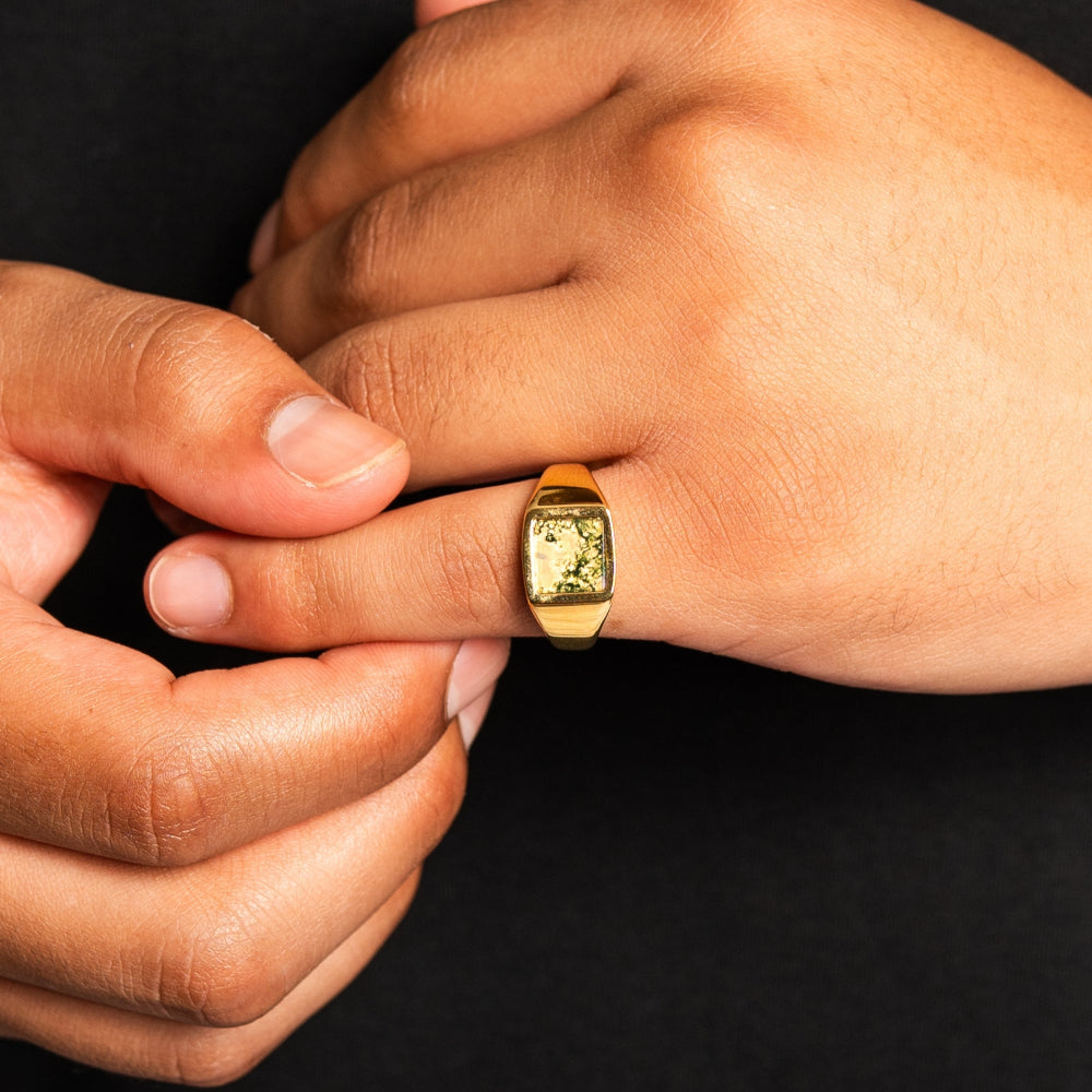 Close-up of a hand wearing a gold ring with a black background