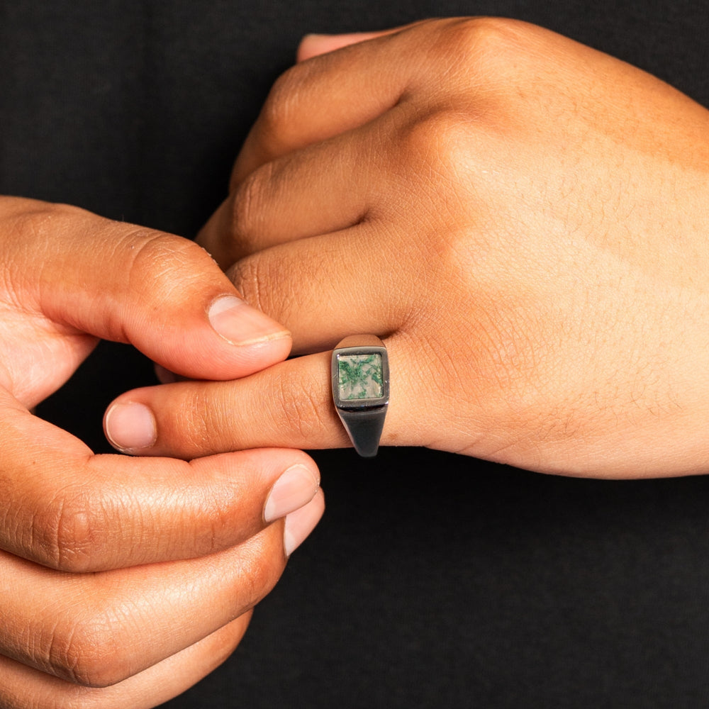 Close-up of a hand wearing a ring with a green gemstone against a black background