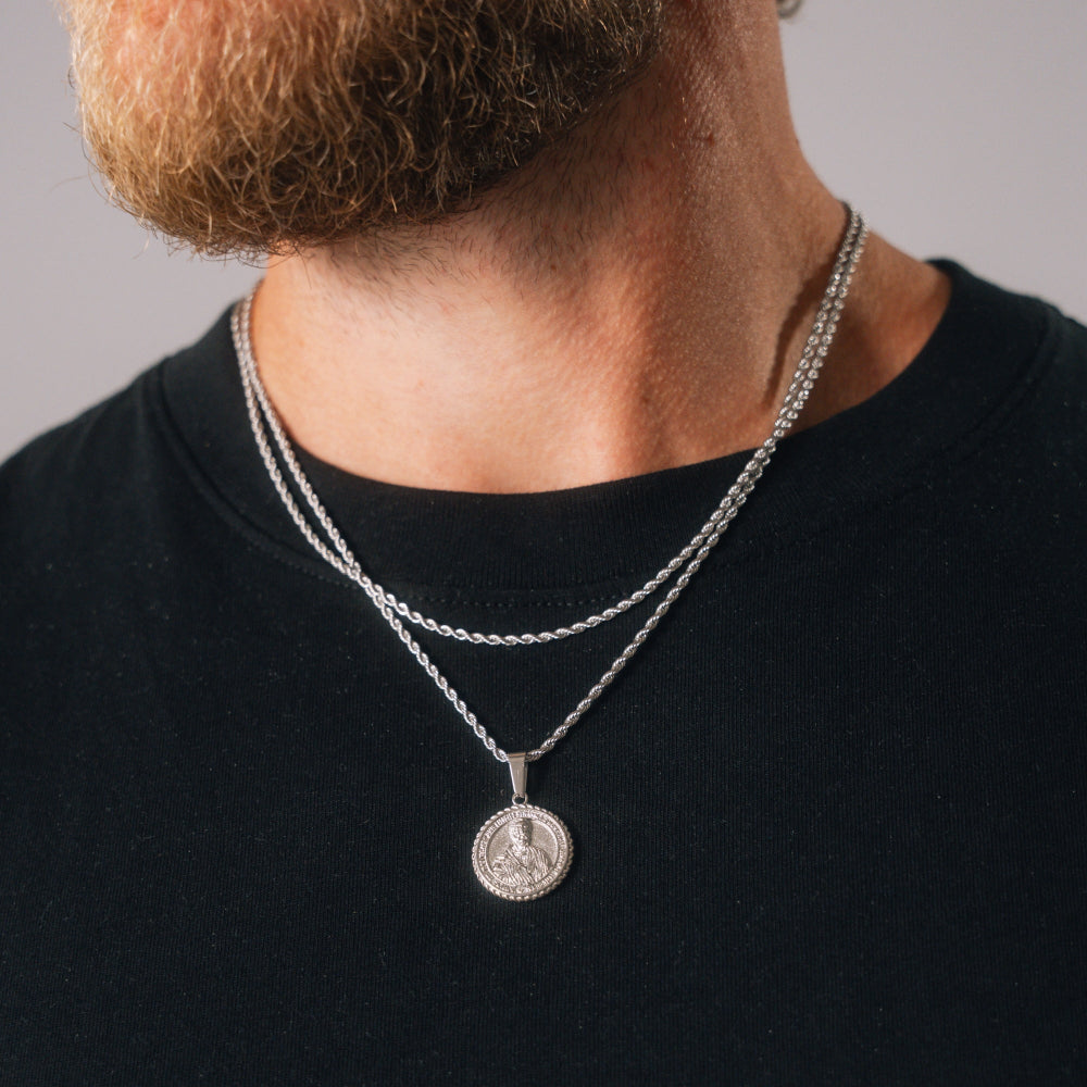 Person wearing a silver necklace with a pendant on a plain background