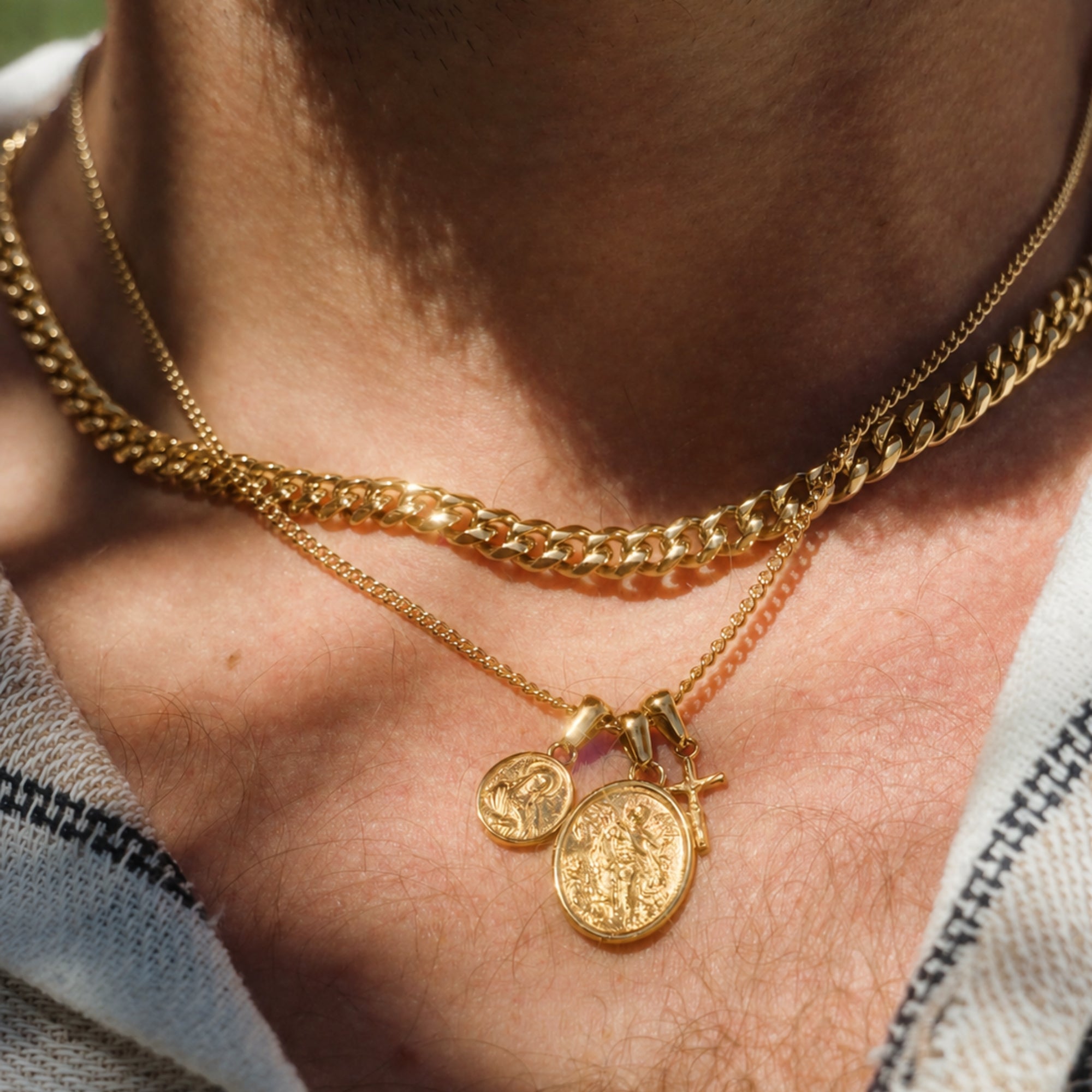 Close-up of a person wearing two gold necklaces with coins and a cross pendant.