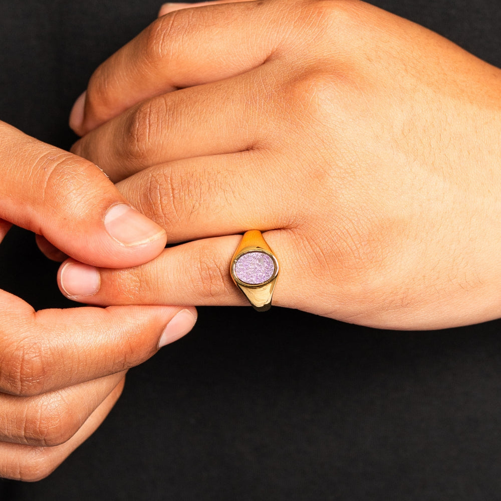 Close-up of a hand wearing a gold ring with a purple gemstone on a black background