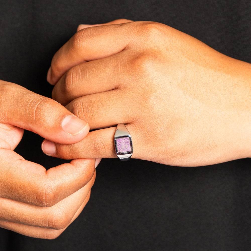 Close-up of a hand wearing a ring with a purple gemstone on a black background