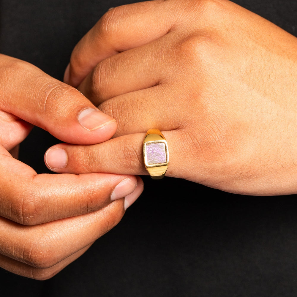 Close-up of a hand wearing a gold ring with a pink stone on a black background