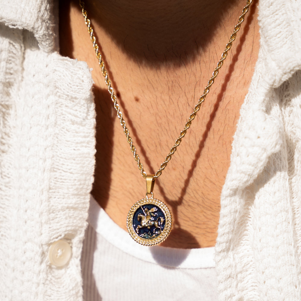 Gold necklace with a detailed pendant worn by a person in a white outfit.