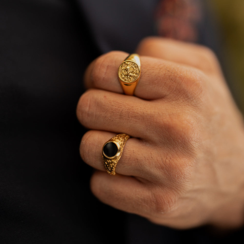 Close-up of a hand wearing two gold rings with black stones on a blurred background