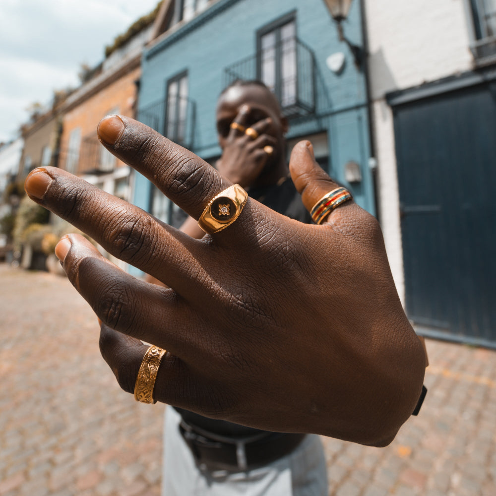 Close-up of a person's hands with gold rings, blurred street scene in the background