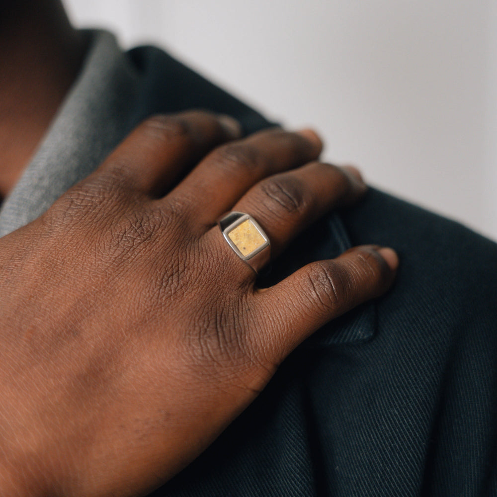 Hand wearing a gold ring on a dark fabric background