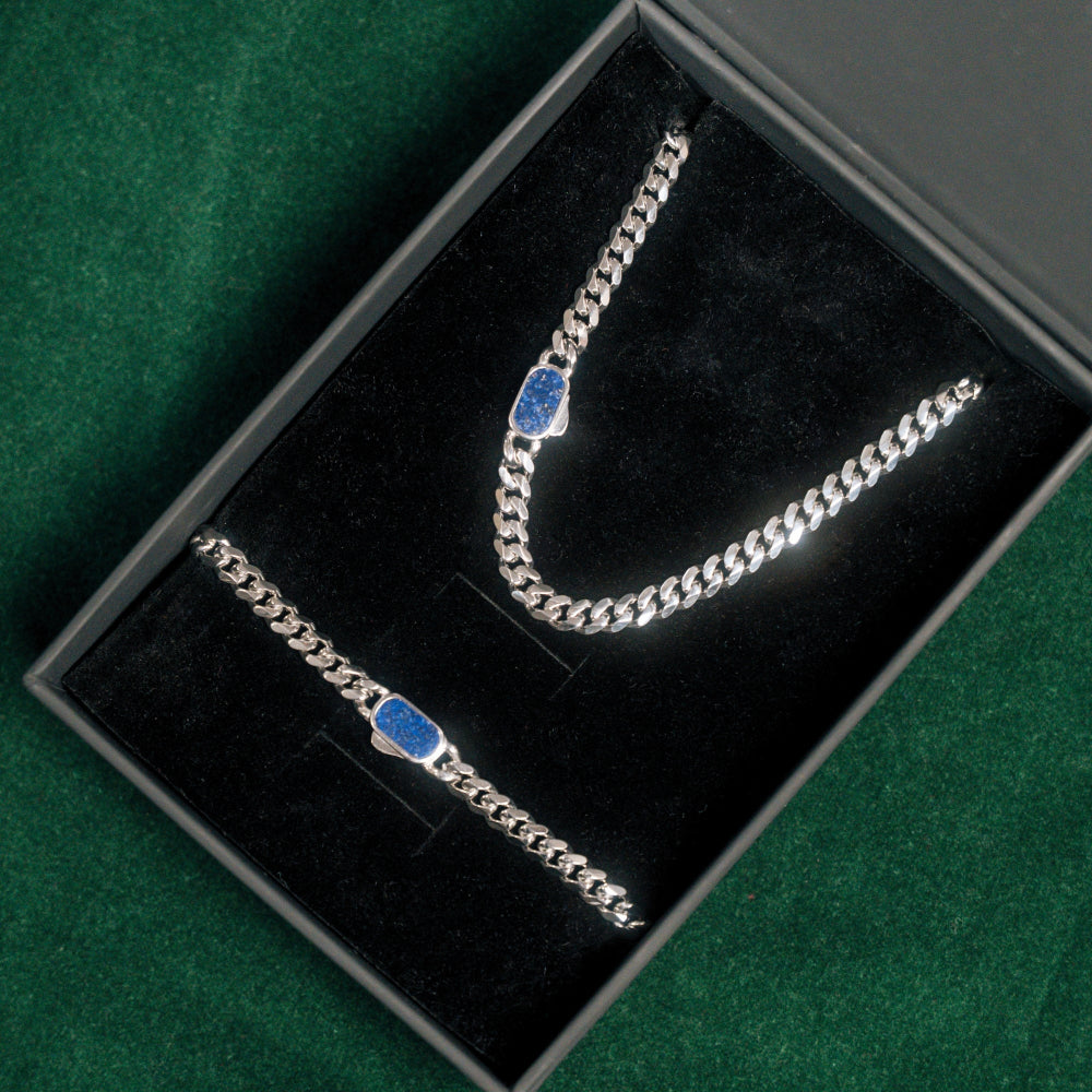 Silver chain necklace with blue stones in a black jewelry box on a green surface