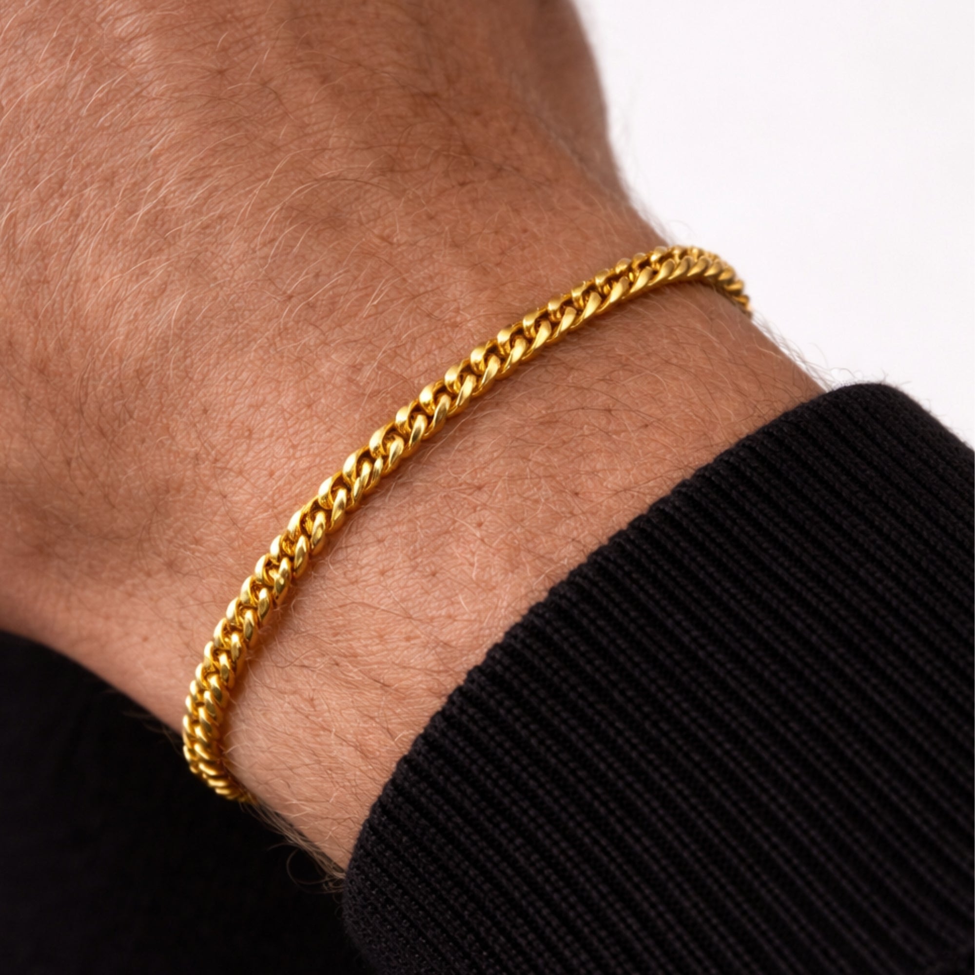 Gold chain bracelet on a wrist with a black sleeve against a white background