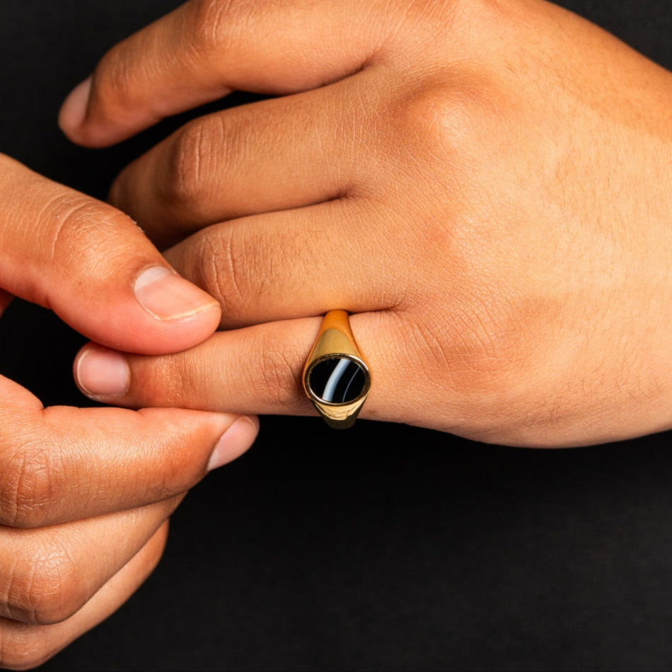 Close-up of a hand wearing a gold ring with a black stone on a dark background