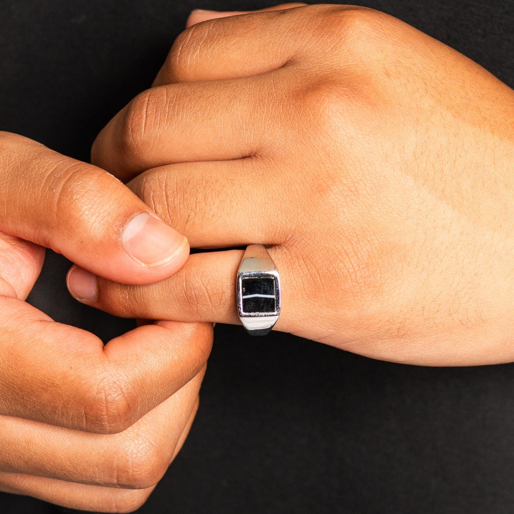 Close-up of a hand wearing a silver ring with a black stone on a dark background