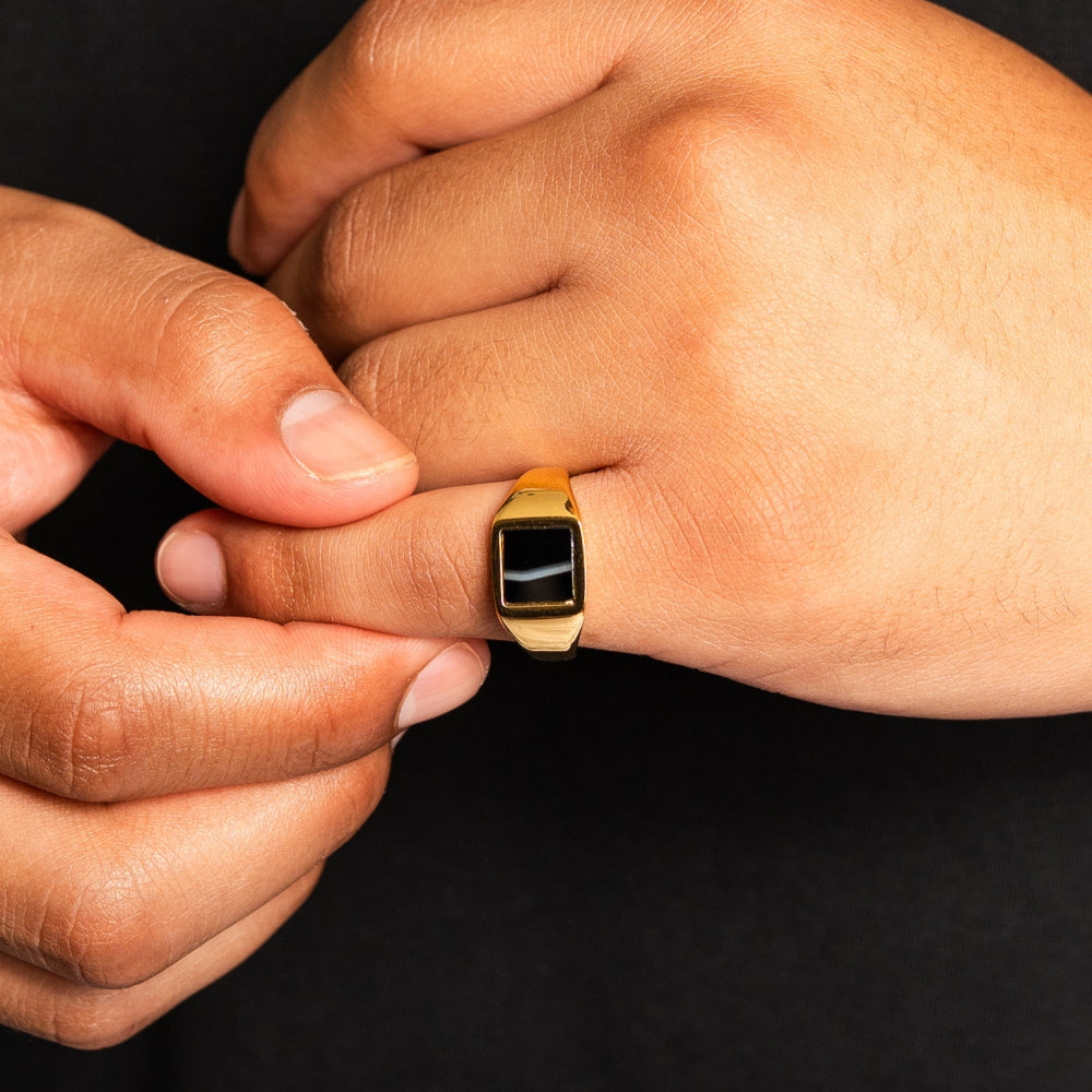 Gold ring being adjusted on a finger against a black background