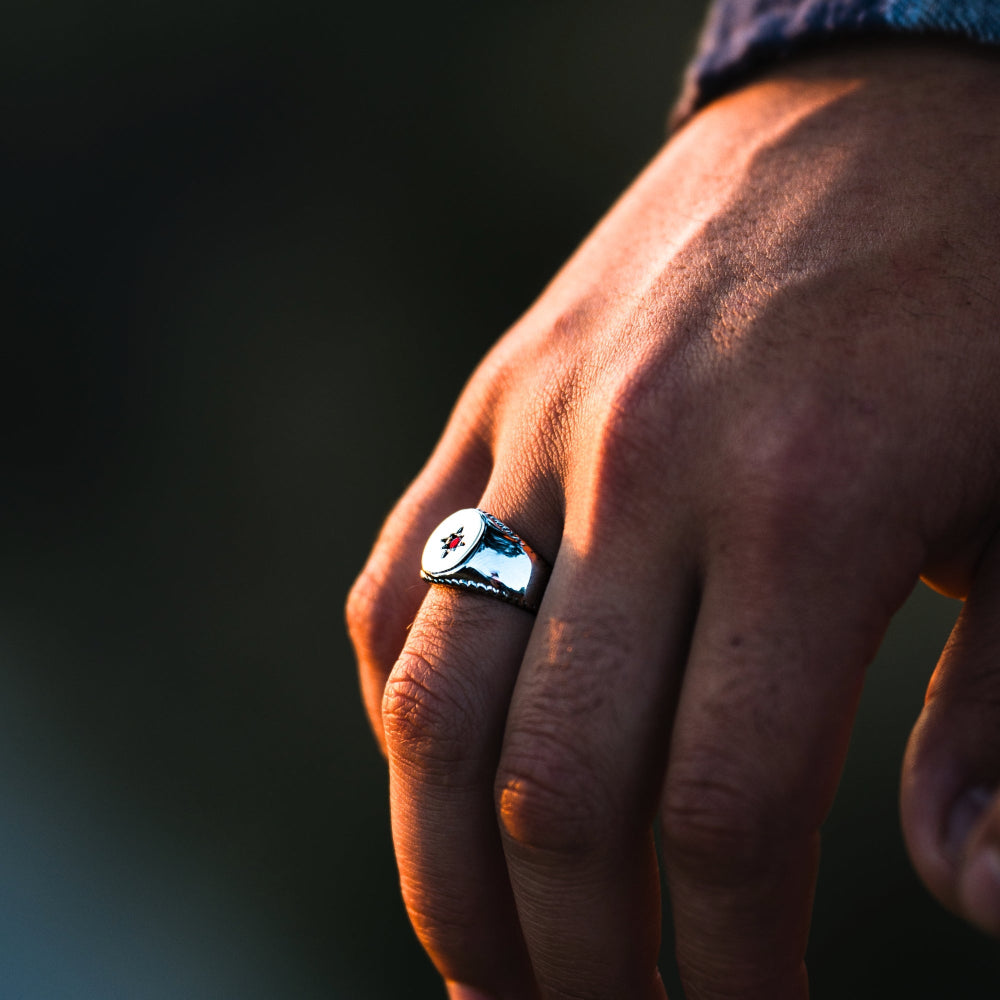 Hand wearing a ring with a logo against a dark background
