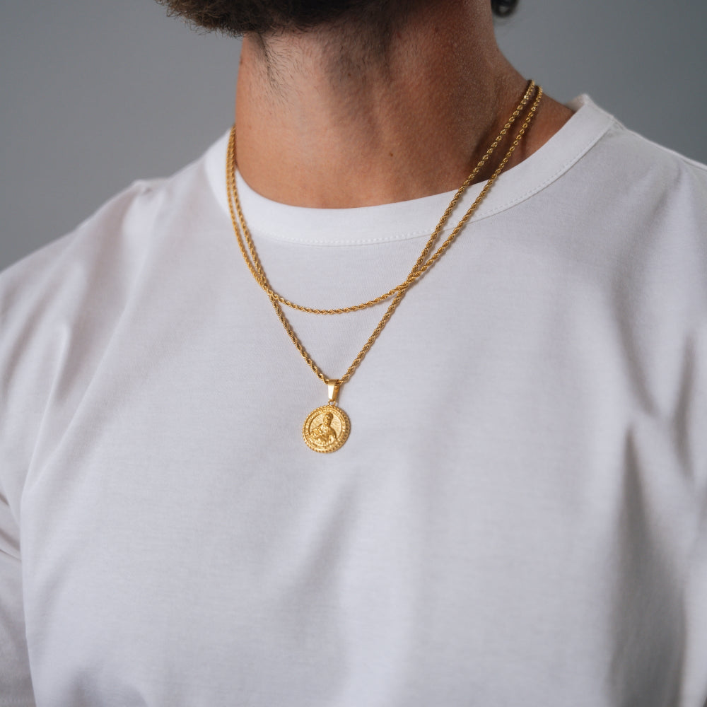 Person wearing a gold necklace with a coin pendant on a plain background
