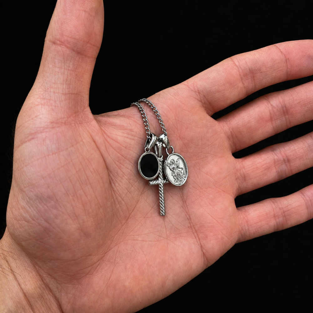 Hand holding a silver necklace with three charms against a black background