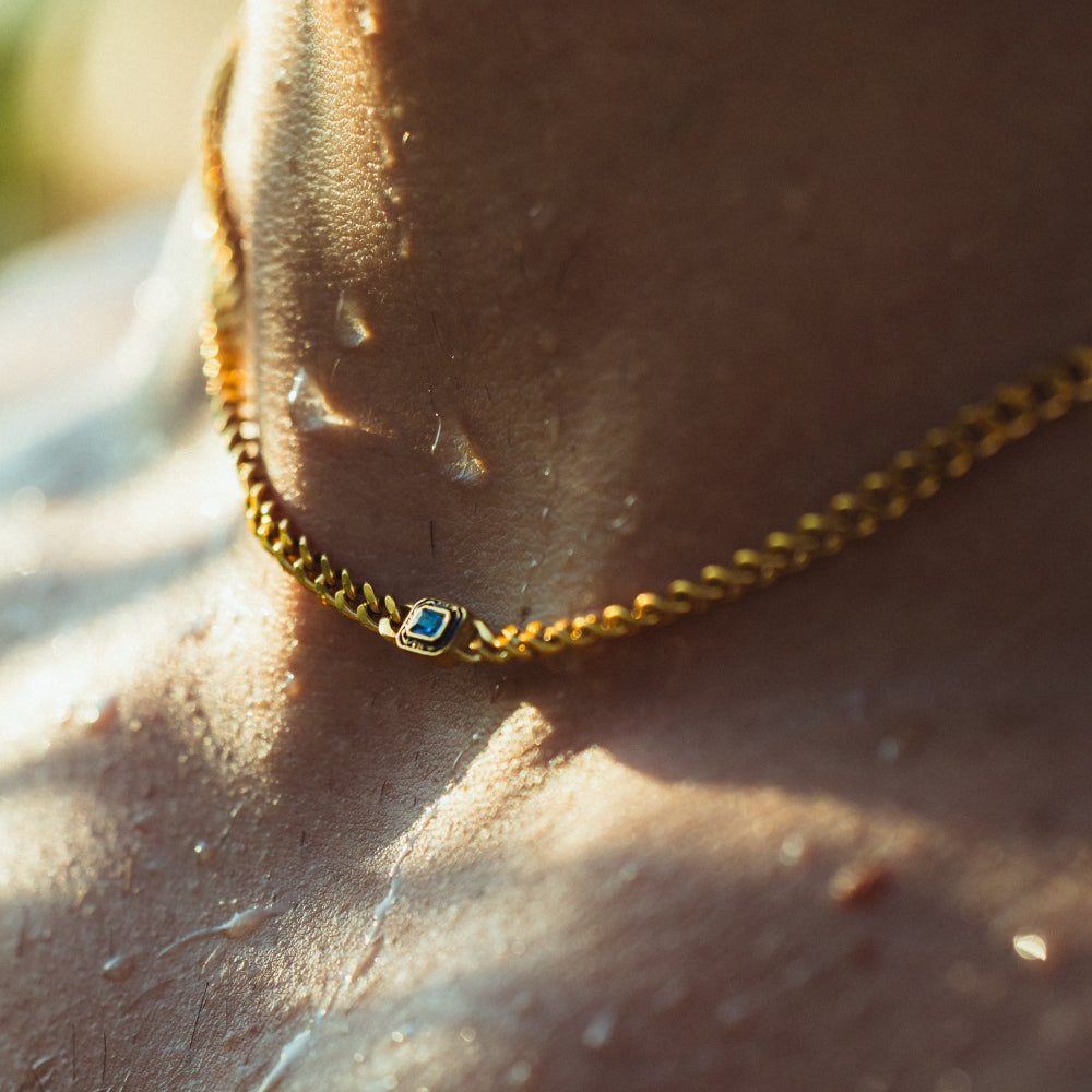 Gold chain bracelet with a blue gemstone on a person's wrist.
