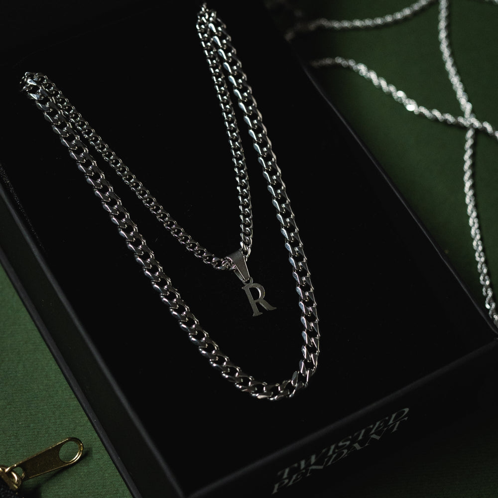 Silver chain necklace with a letter 'R' pendant on a black box with a brand name.