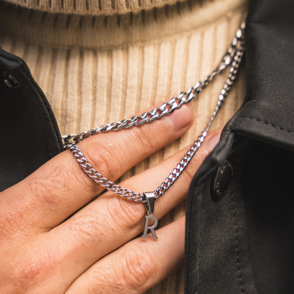 Hand wearing a silver chain necklace with a 'R' pendant.