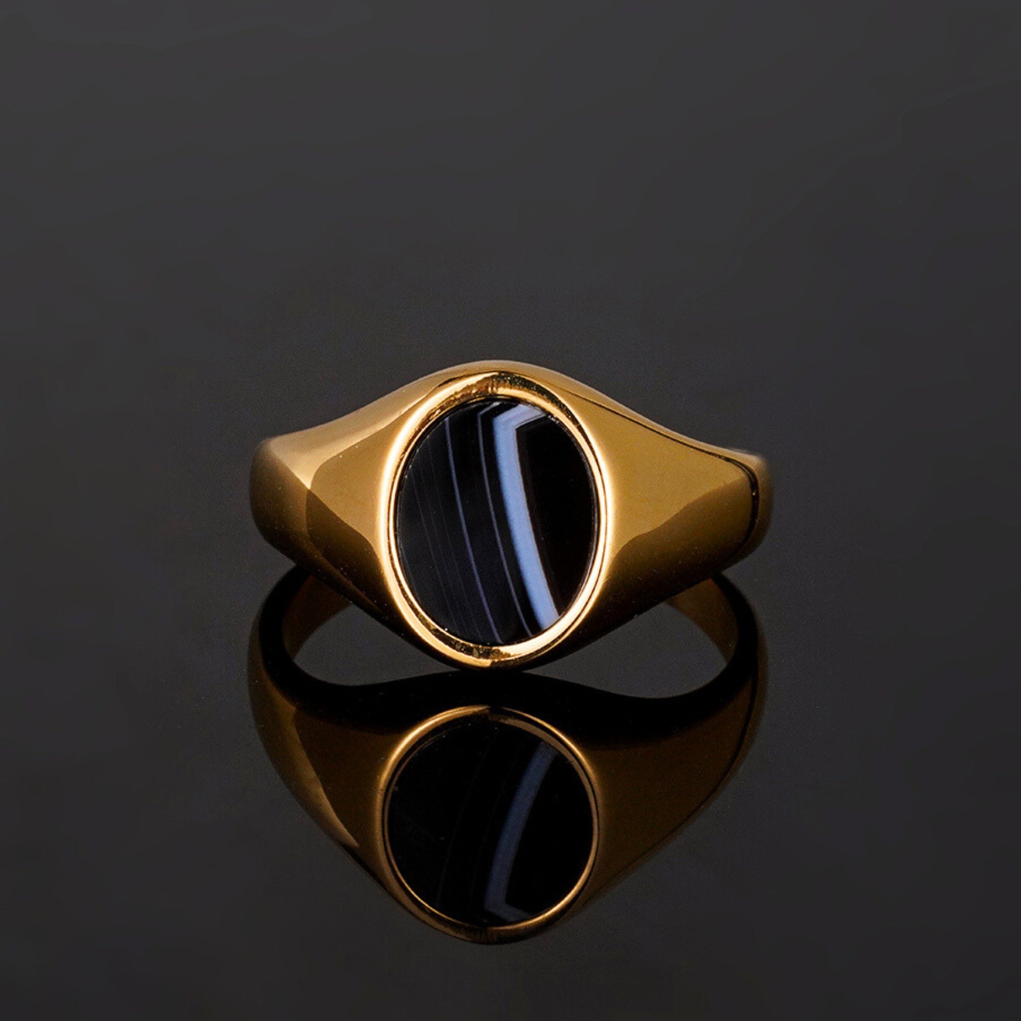 Gold ring with a black stone on a reflective black surface