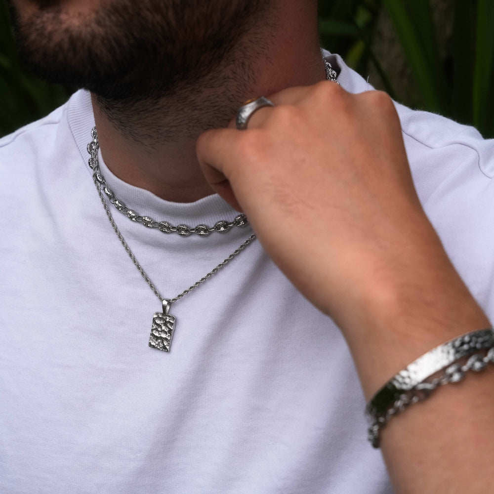 Person adjusting a silver chain necklace with a pendant on a white shirt.