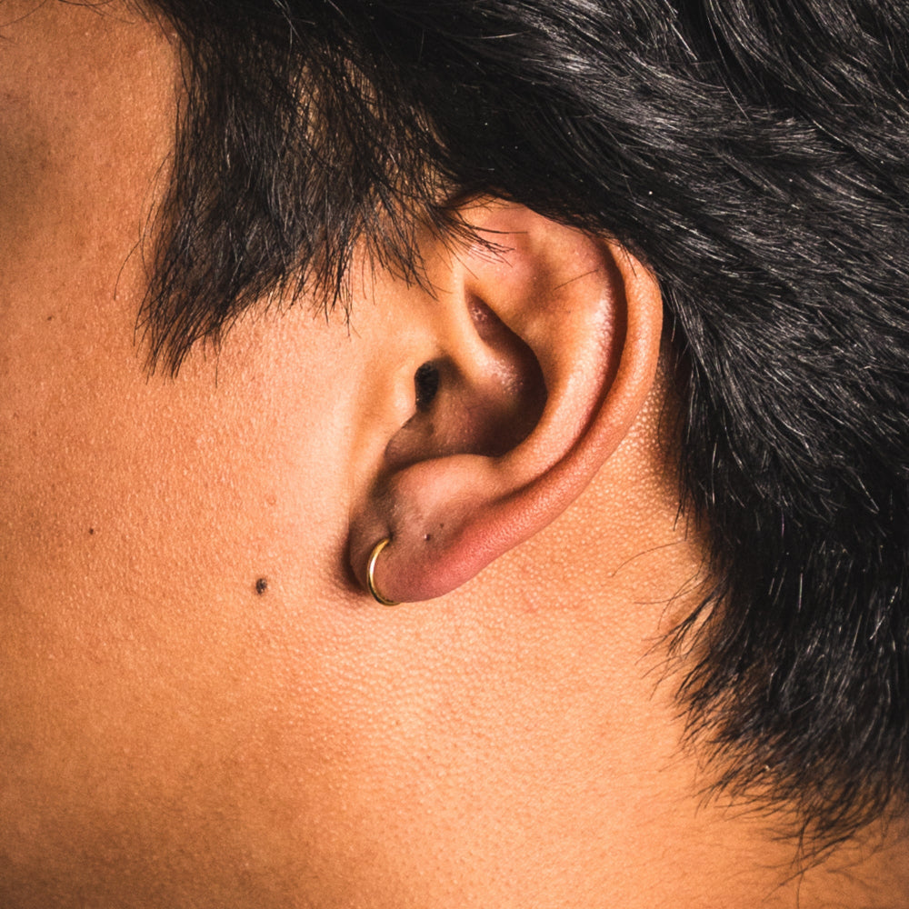 Close-up of an ear with a gold hoop earring on a person with dark hair.