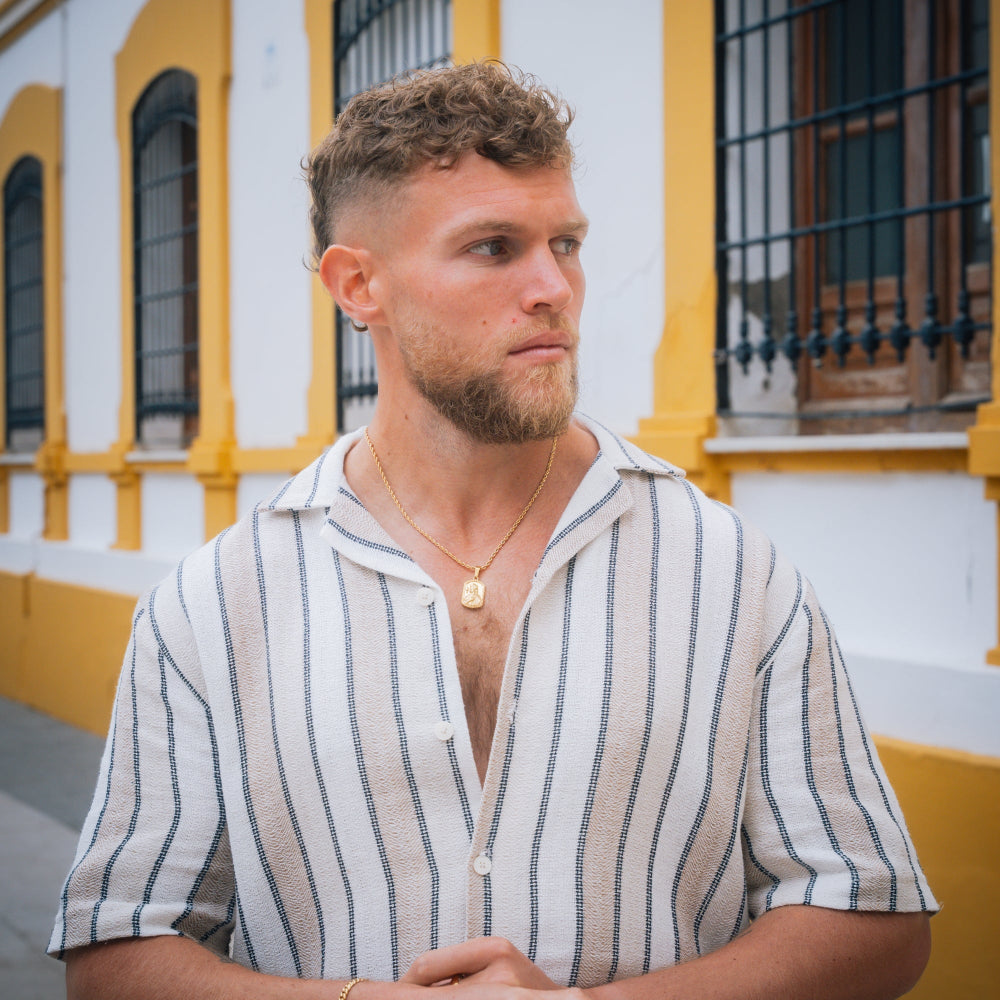 Man wearing a striped shirt standing in front of a yellow and white building.