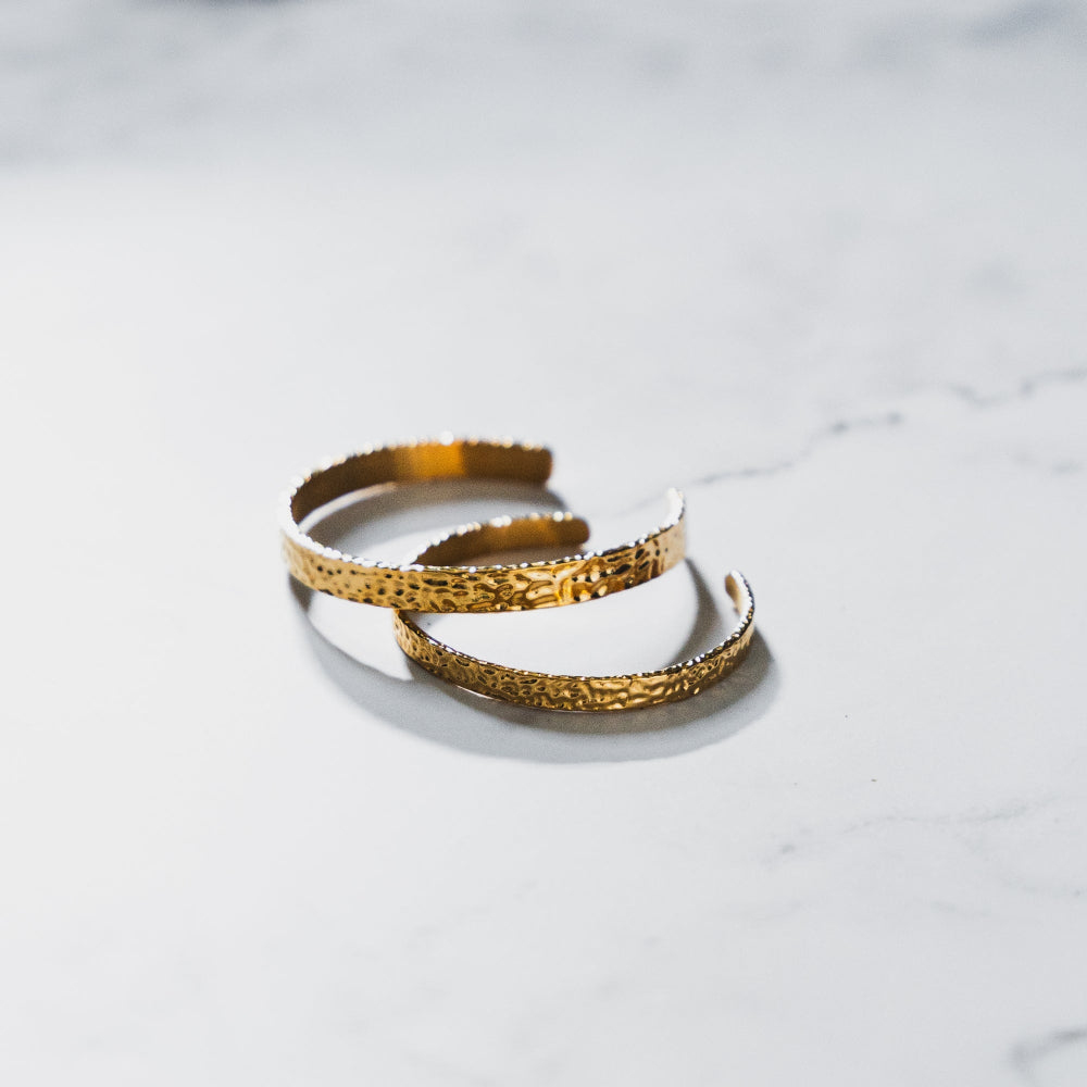 Two gold bracelets on a light marble surface