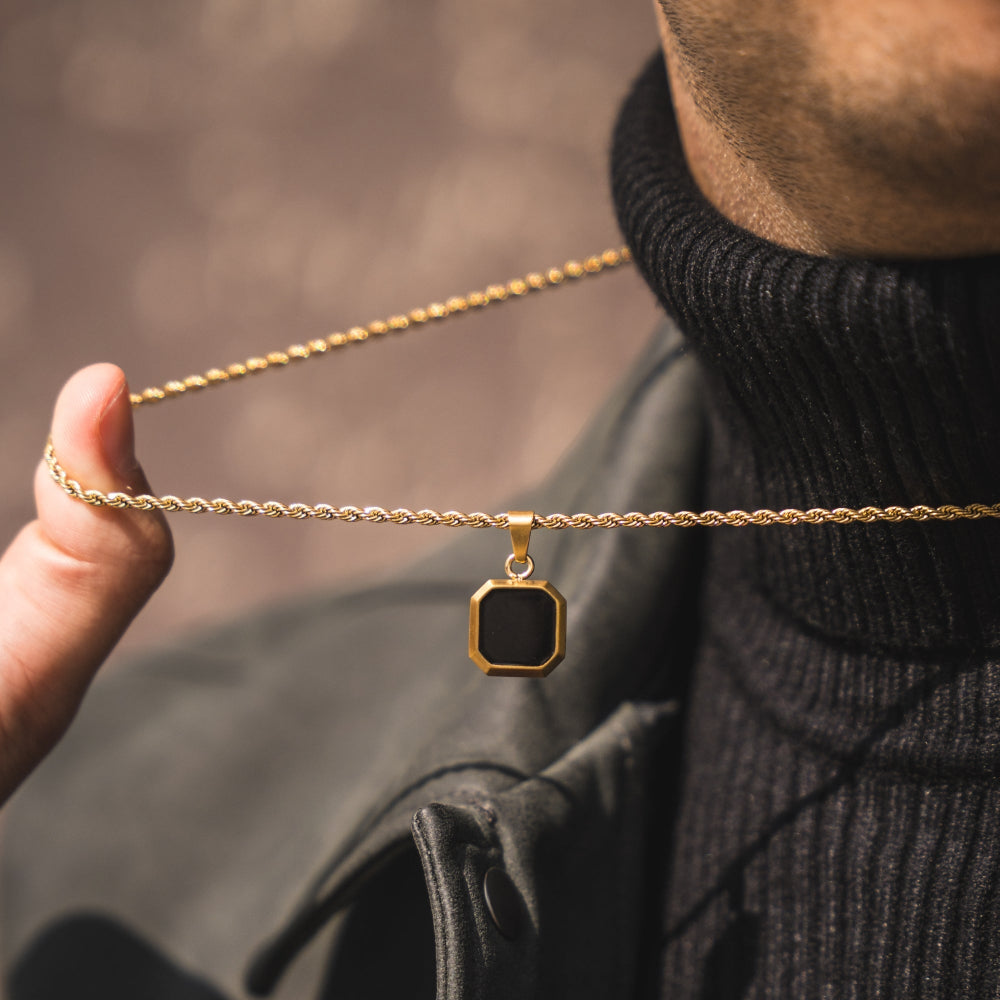 Gold necklace with a black pendant held by a person wearing a black sweater.