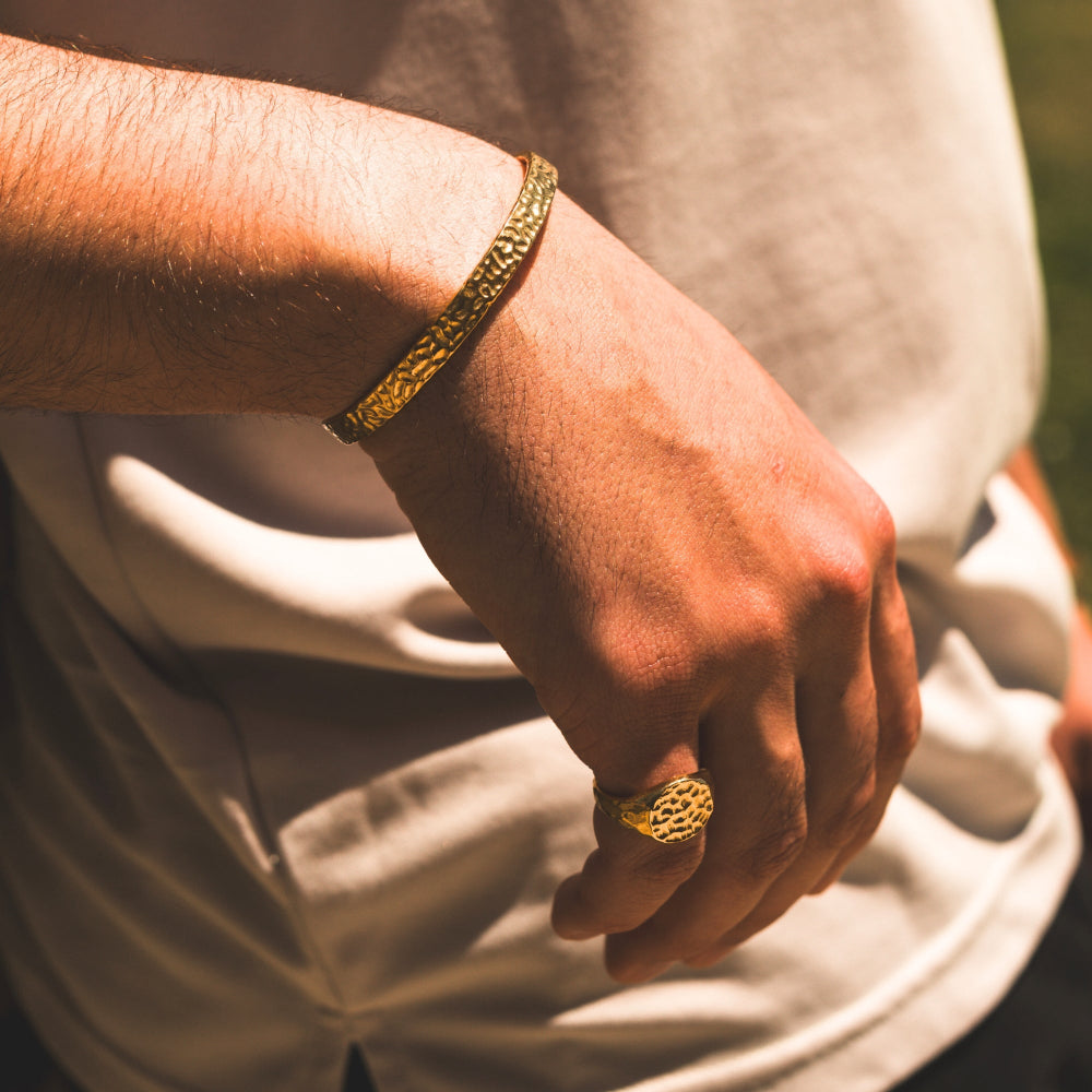 Close-up of a person's wrist wearing a gold bracelet and ring, with a blurred background.