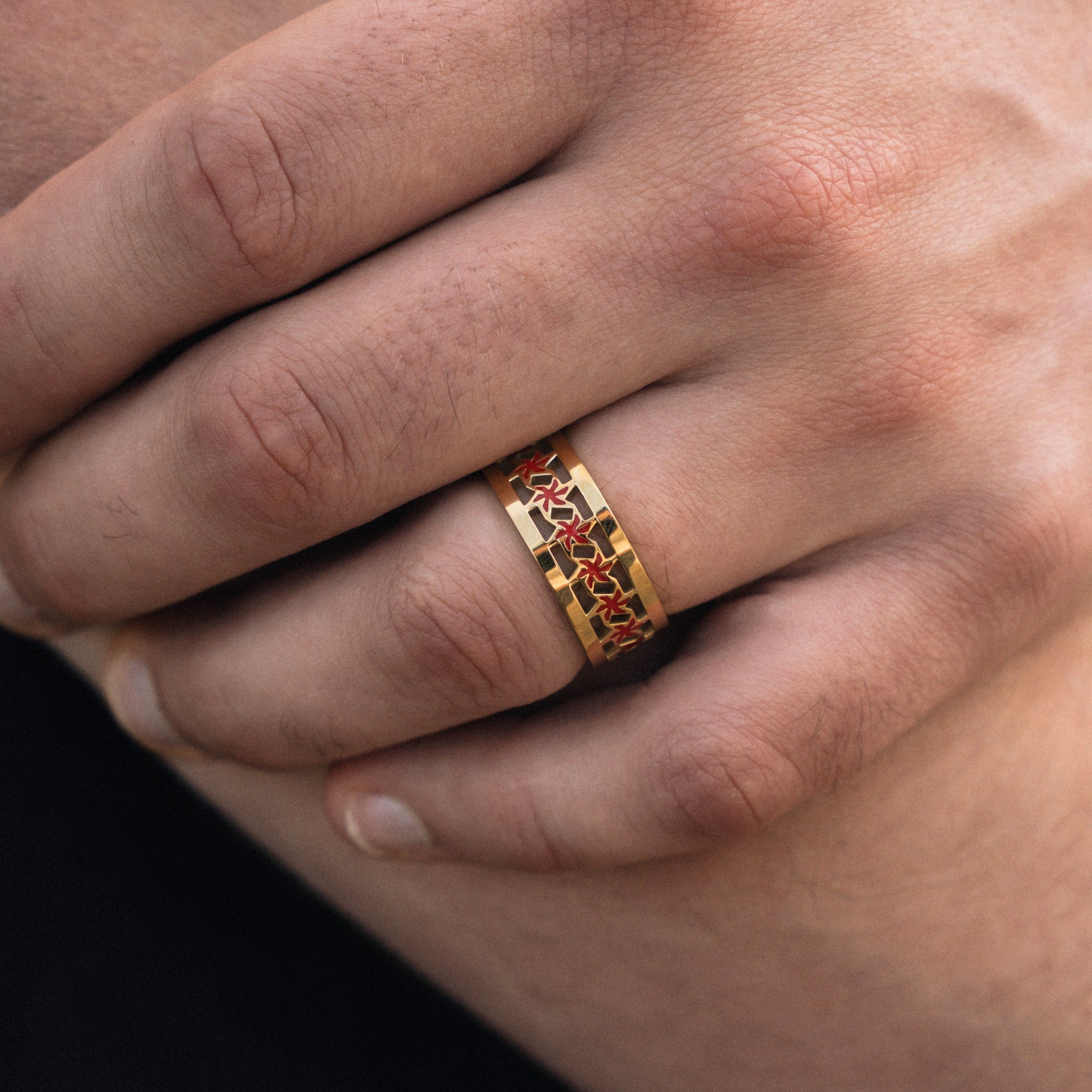 Gold ring with red accents on a person's finger against a neutral background