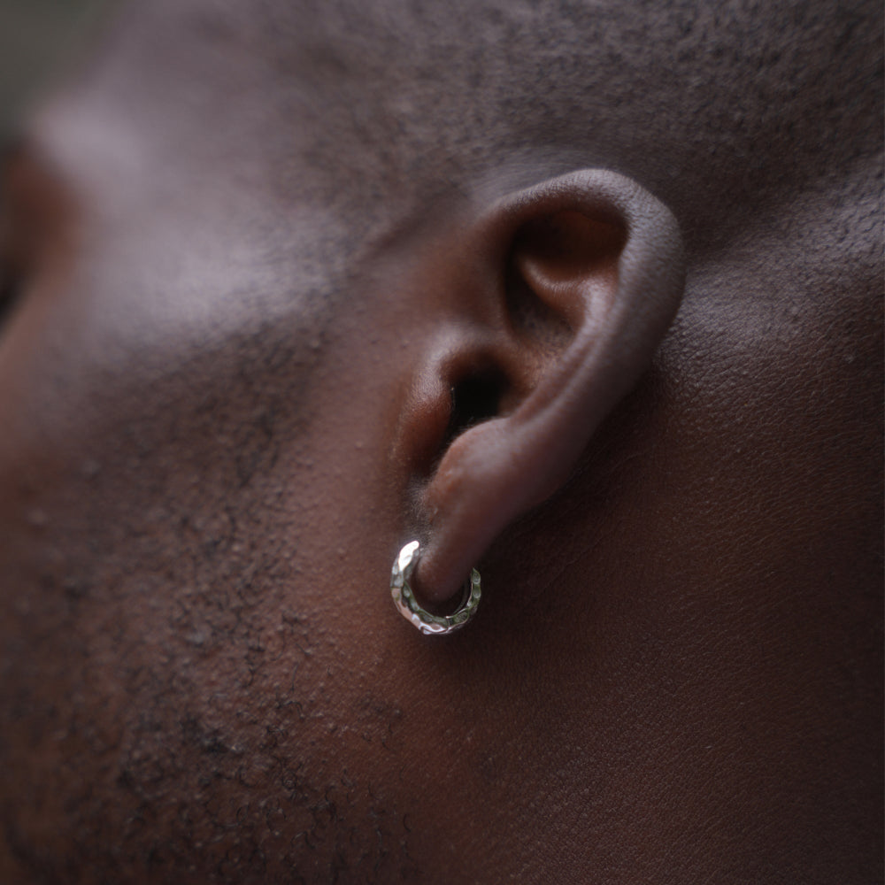 Close-up of an ear with a silver hoop earring on a dark background